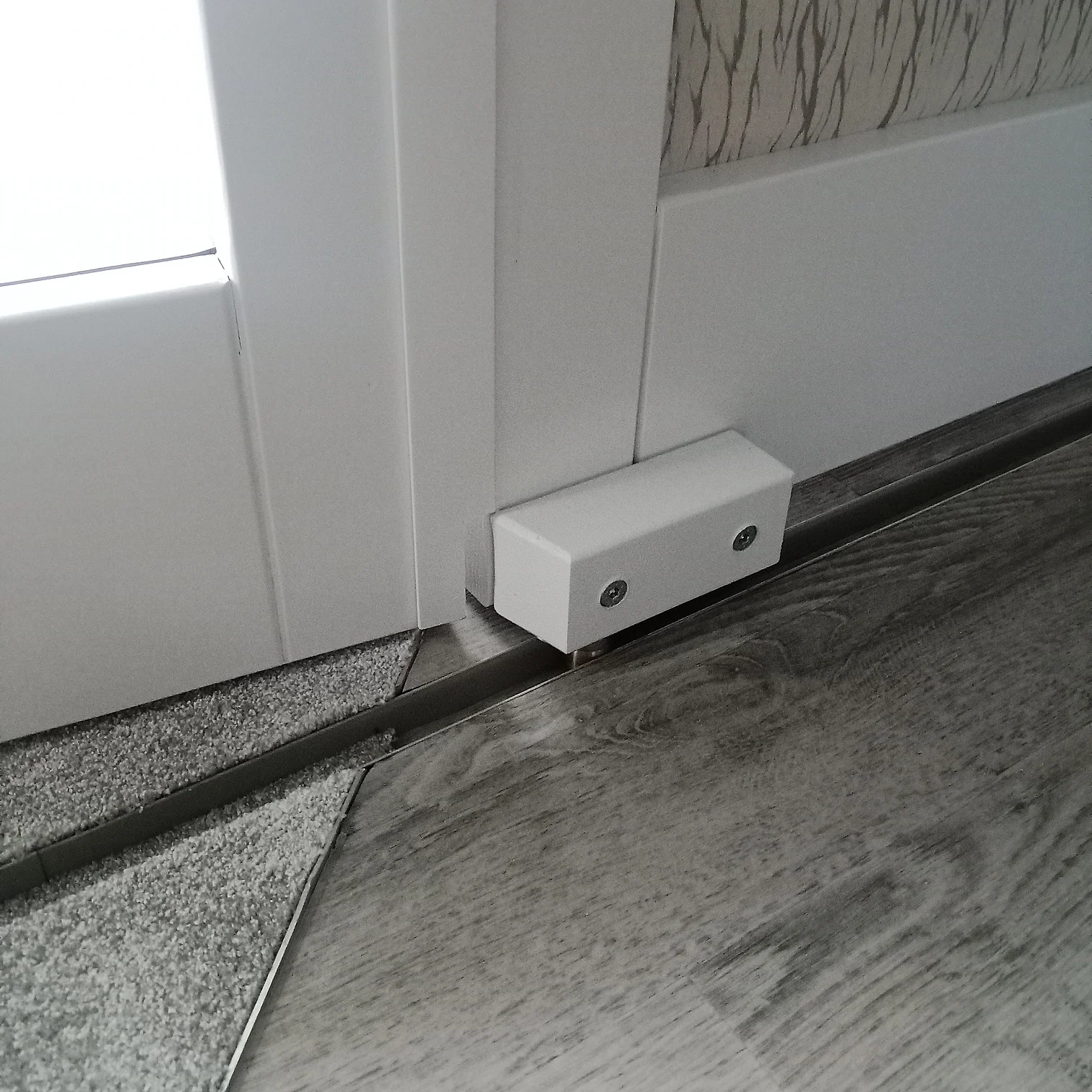 Bodenführung für Schiebetür auf dunklem Laminat vor weißer Wand